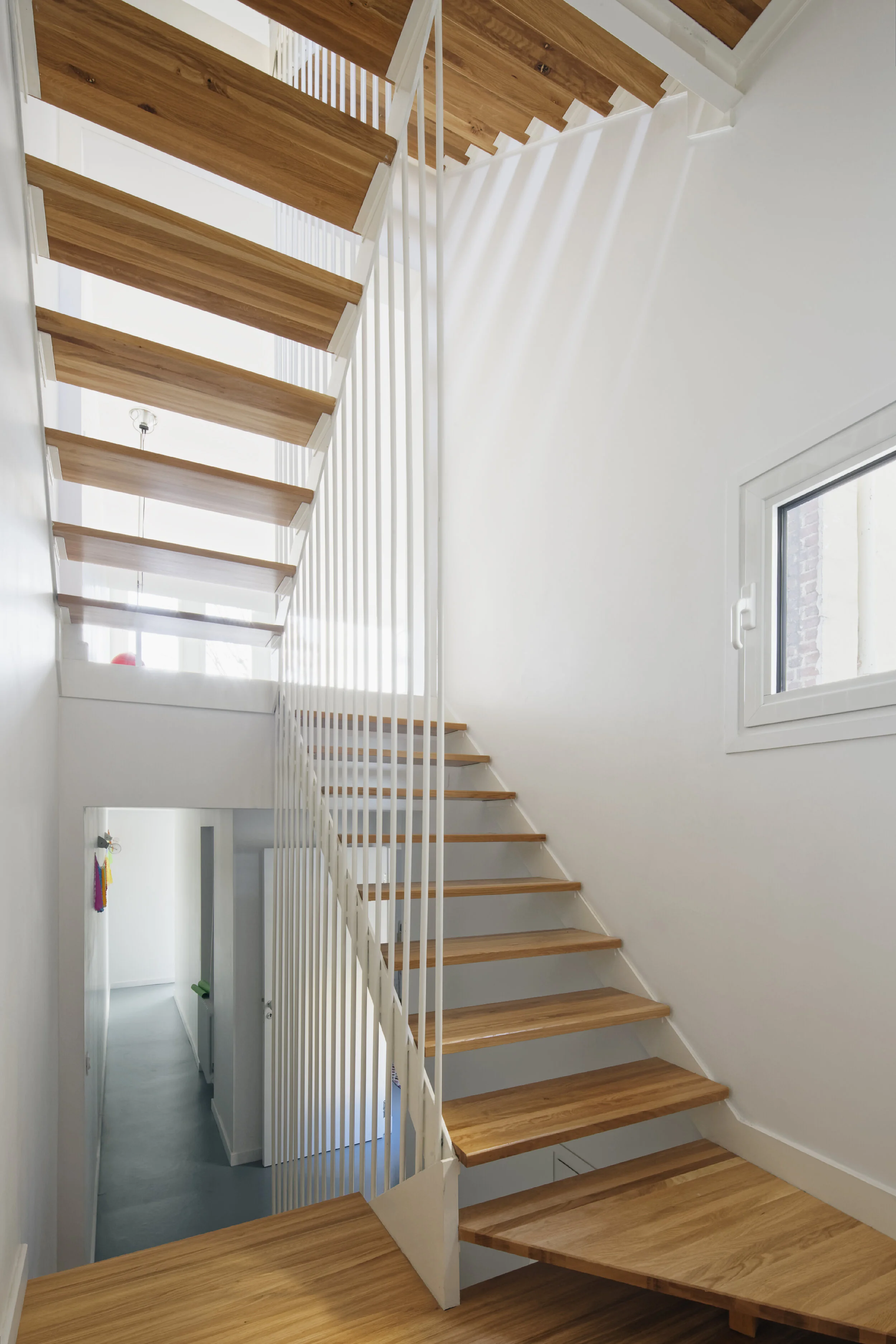 Cage d'escalier centrale — volée unique reliant les cinq étages, contraste bois clair et parois blanches